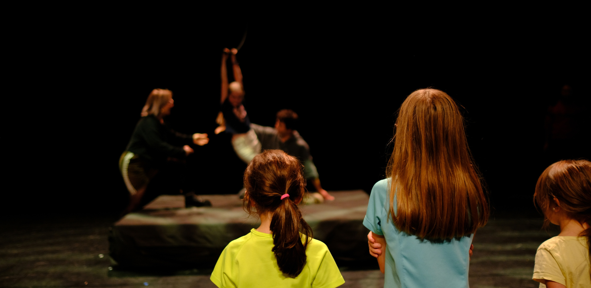 trois enfants de dos regardent une petite fille qui participe à un atelier de cirque, encadré de deux adultes