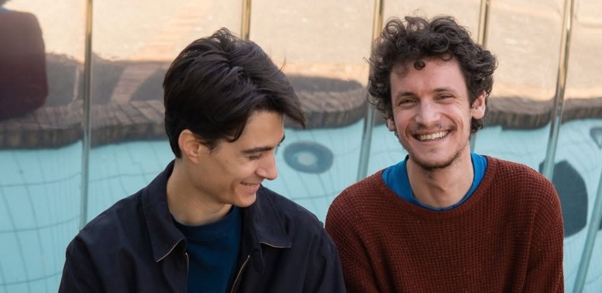 deux hommes assis côte à côte et souriants
